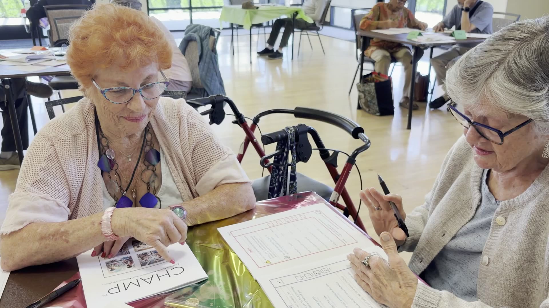 Two friends at a CHAMP cognitive health workshop, one with the booklet, one completing the assessment